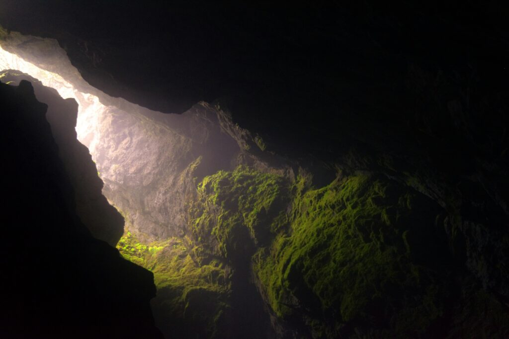Sunlight streams into a dark cave with moss-covered walls in Smoljan, Bulgaria.