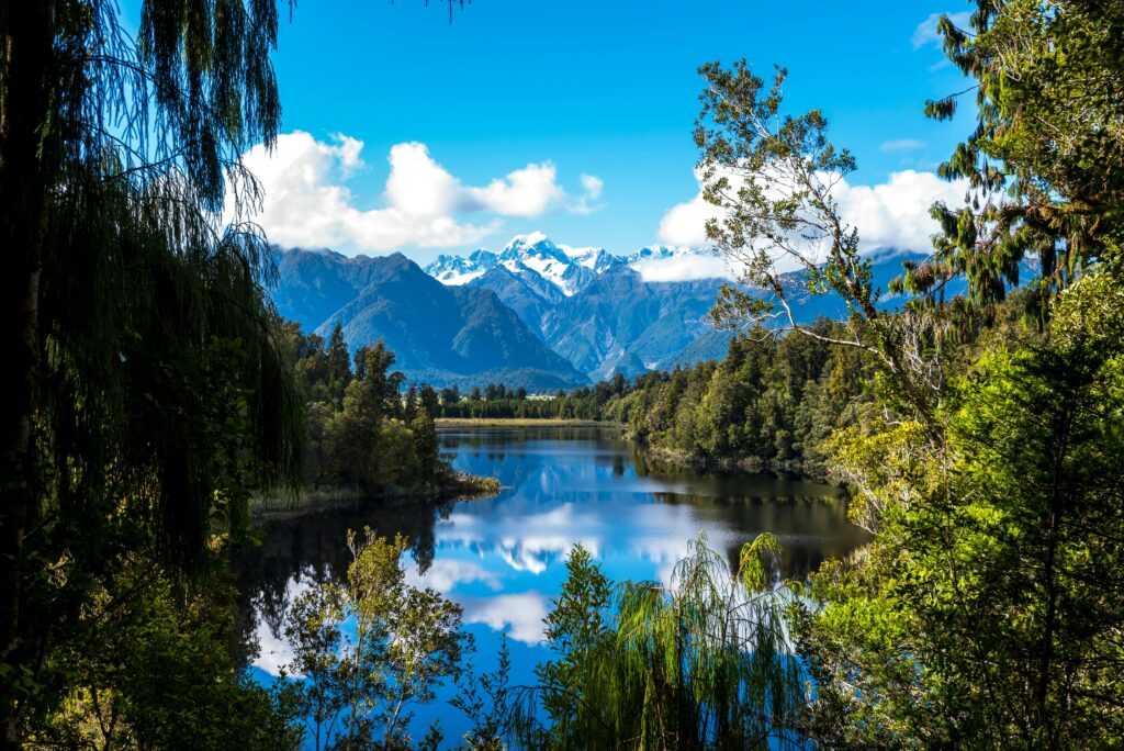 Stunning view of a clear lake surrounded by snow-capped mountains and lush forest.