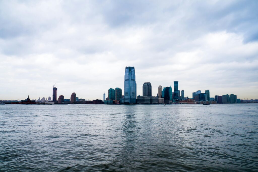 Dramatic view of Jersey City's skyline under a cloudy sky across the Hudson River.